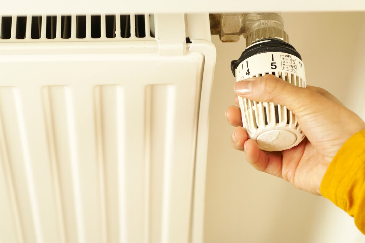Hand stellt Thermostatventil an einem Heizkörper ein